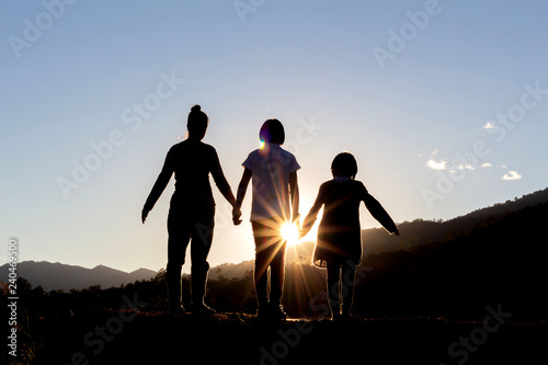 Silhouettes of happy mother and daughters looking morning sunrise on peak of mountain.