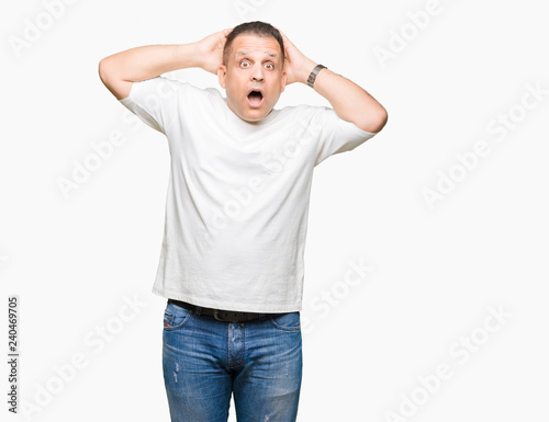 Middle age arab man wearig white t-shirt over isolated background Crazy and scared with hands on head, afraid and surprised of shock with open mouth