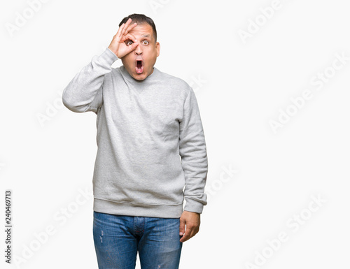 Middle age arab man wearing sport sweatshirt over isolated background doing ok gesture shocked with surprised face, eye looking through fingers. Unbelieving expression.