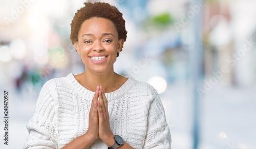 Beautiful young african american woman wearing sweater over isolated background praying with hands together asking for forgiveness smiling confident.