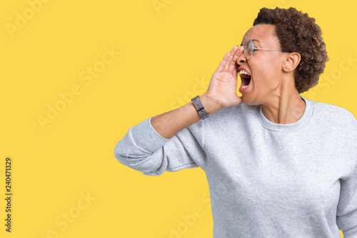 Young beautiful african american woman wearing glasses over isolated background shouting and screaming loud to side with hand on mouth. Communication concept.
