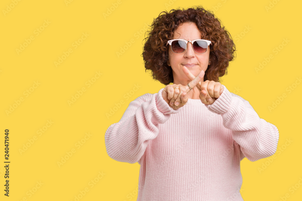 Beautiful middle ager senior woman wearing pink sweater and sunglasses over isolated background Rejection expression crossing fingers doing negative sign Beautiful middle ager senior woman wearing pink sweater and sunglasses over isolated background Rejection expression crossing fingers doing negative sign
