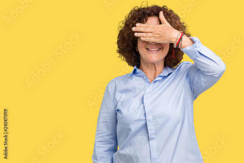 Beautiful middle ager senior businees woman wearing glasses over isolated background smiling and laughing with hand on face covering eyes for surprise. Blind concept.