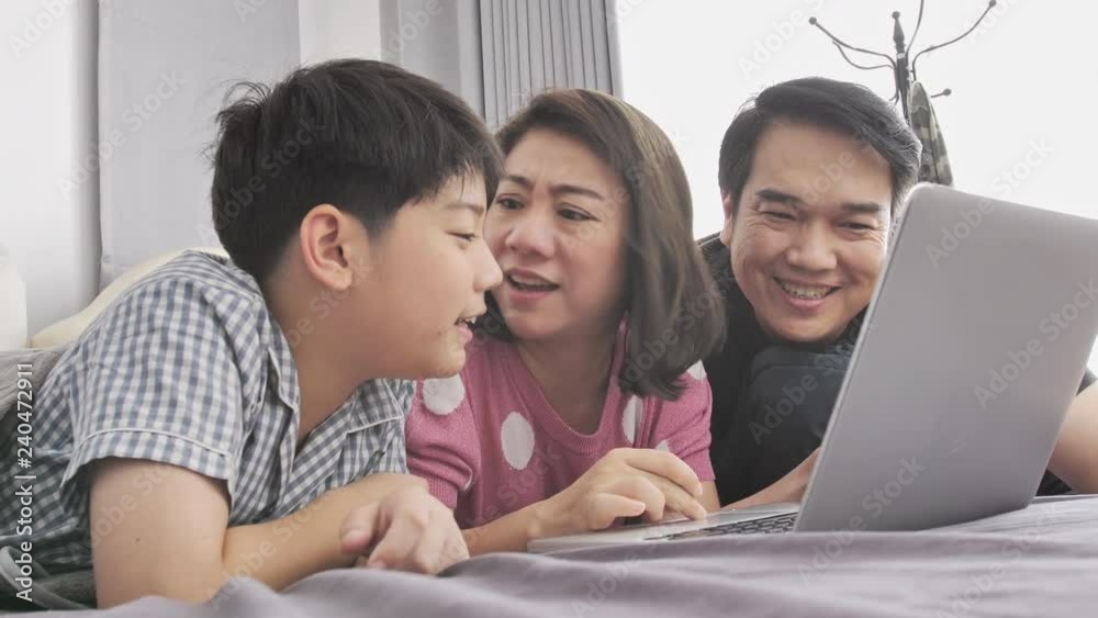 Happy family Father mother and son watching on laptop computer and having fun, Slow motion 4K asian family rest on bed with laptop computer Happy family Father mother and son watching on laptop computer and having fun, Slow motion 4K asian family rest on bed with laptop computer