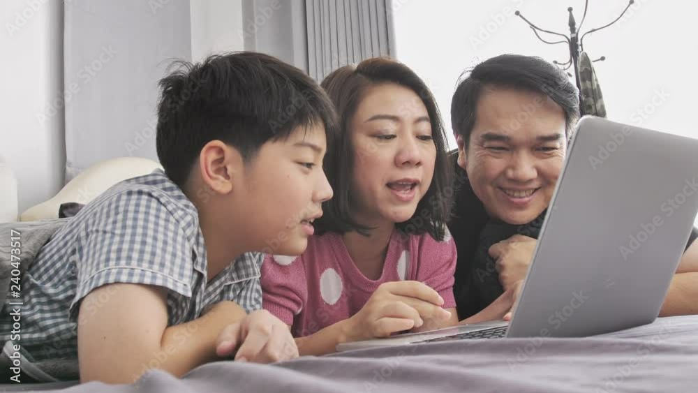 Happy family Father mother and son watching on laptop computer and having fun, Slow motion 4K asian family rest on bed with laptop computer Happy family Father mother and son watching on laptop computer and having fun, Slow motion 4K asian family rest on bed with laptop computer