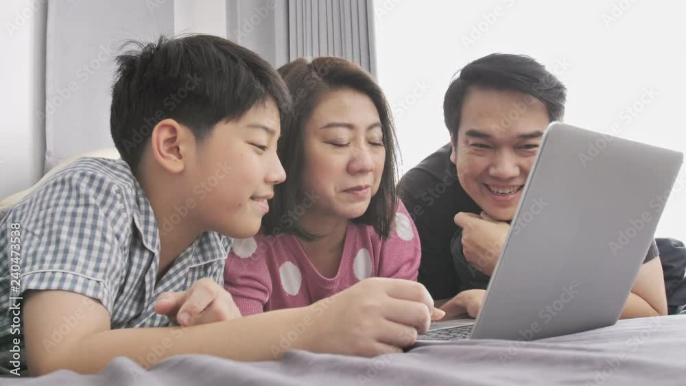 Happy family Father mother and son watching on laptop computer and having fun, Slow motion 4K asian family rest on bed with laptop computer Happy family Father mother and son watching on laptop computer and having fun, Slow motion 4K asian family rest on bed with laptop computer