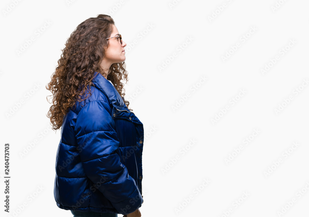 Beautiful young brunette curly hair girl wearing winter coat, glasses and sweater over isolated background looking to side, relax profile pose with natural face with confident smile. Beautiful young brunette curly hair girl wearing winter coat, glasses and sweater over isolated background looking to side, relax profile pose with natural face with confident smile.