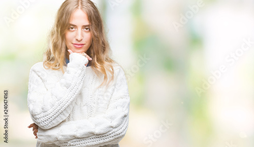 Beautiful young blonde woman wearing winter sweater over isolated background looking confident at the camera with smile with crossed arms and hand raised on chin. Thinking positive. © Krakenimages.com