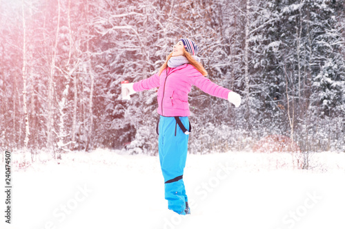 Beautiful happy laughing red-haired young woman in a winter tracksuit covered in snow flakes. Winter forest landscape background.