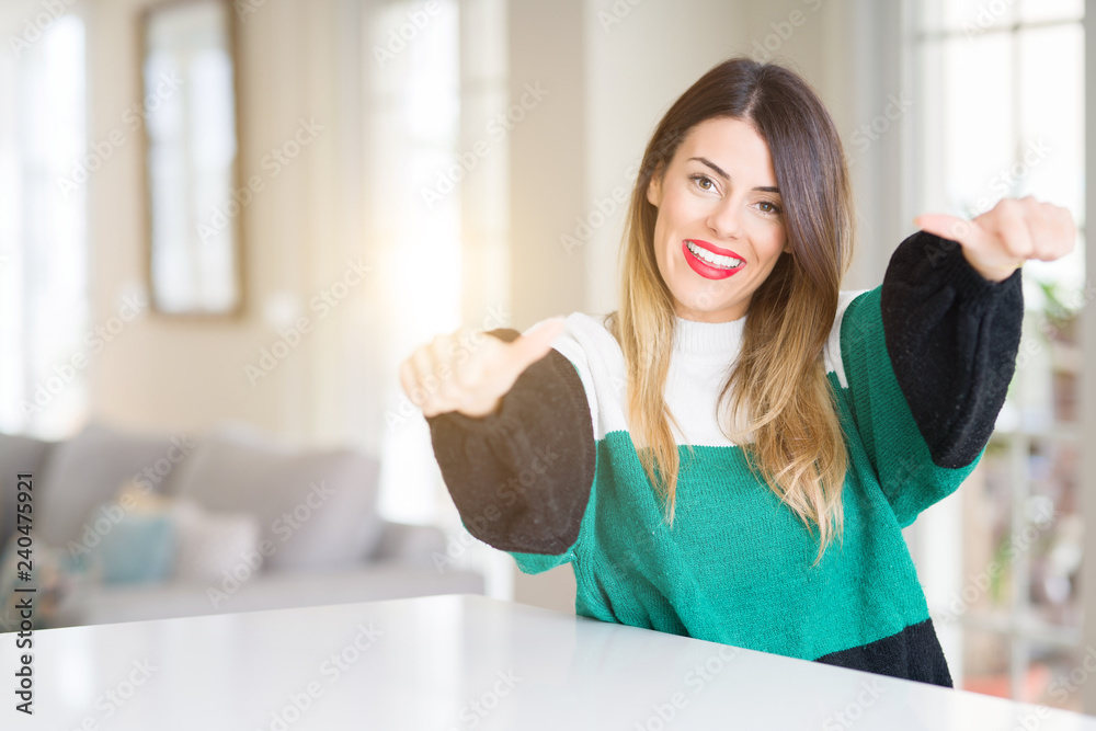 Young beautiful woman wearing winter sweater at home approving doing positive gesture with hand, thumbs up smiling and happy for success. Looking at the camera, winner gesture. Young beautiful woman wearing winter sweater at home approving doing positive gesture with hand, thumbs up smiling and happy for success. Looking at the camera, winner gesture.