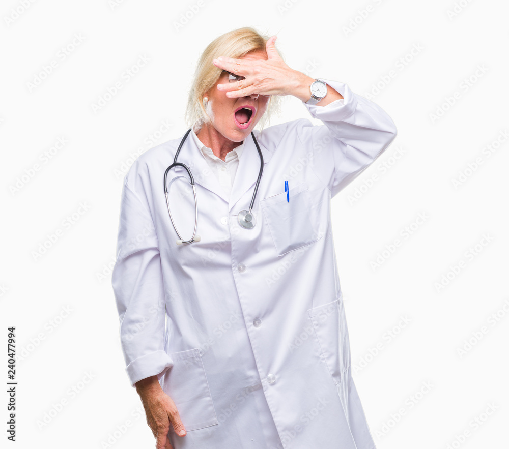 Middle age blonde doctor woman over isolated background peeking in shock covering face and eyes with hand, looking through fingers with embarrassed expression. Middle age blonde doctor woman over isolated background peeking in shock covering face and eyes with hand, looking through fingers with embarrassed expression.