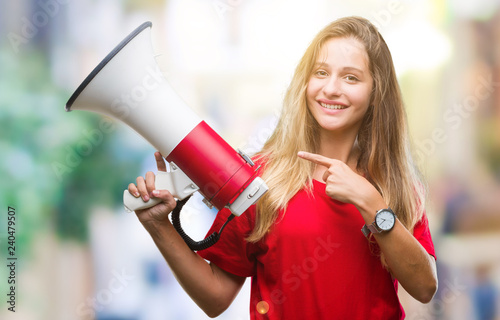 Young beautiful blonde woman yelling through megaphone over isolated background very happy pointing with hand and finger