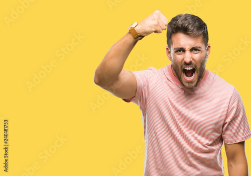 Young handsome man over isolated background angry and mad raising fist frustrated and furious while shouting with anger. Rage and aggressive concept.