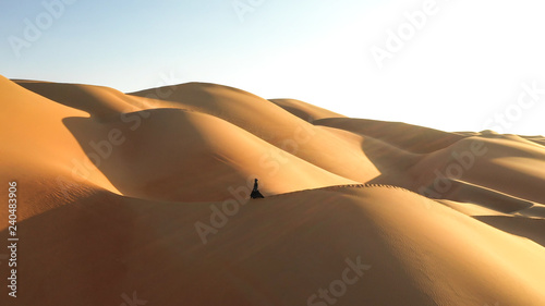 Aerial view from a drone flying next to a woman in abaya  United Arab Emirates traditional dress  walking on the dunes in the desert of the Empty Quarter. Abu Dhabi  UAE.