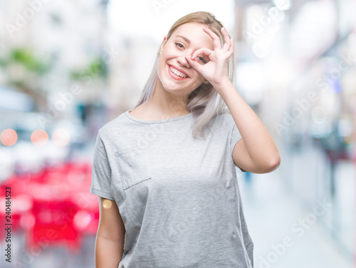 Young blonde woman over isolated background doing ok gesture with hand smiling, eye looking through fingers with happy face.