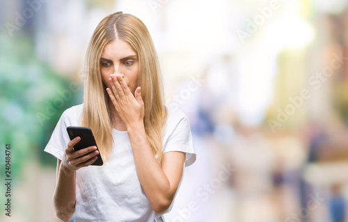 Young beautiful blonde woman using smartphone over isolated background cover mouth with hand shocked with shame for mistake, expression of fear, scared in silence, secret concept