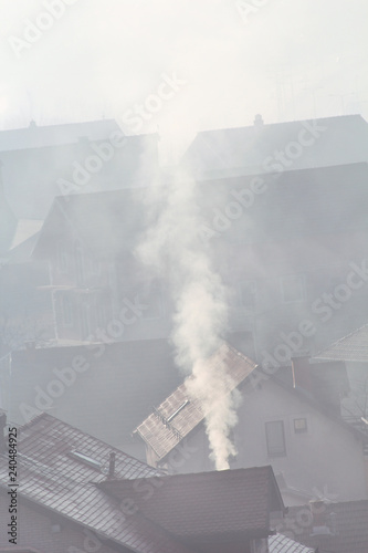 Smoking chimneys at roofs of houses emits smoke, smog at sunrise, pollutants enter atmosphere. Environmental disaster. Harmful emissions and exhaust gases into air. Fog, winter day, heating season.