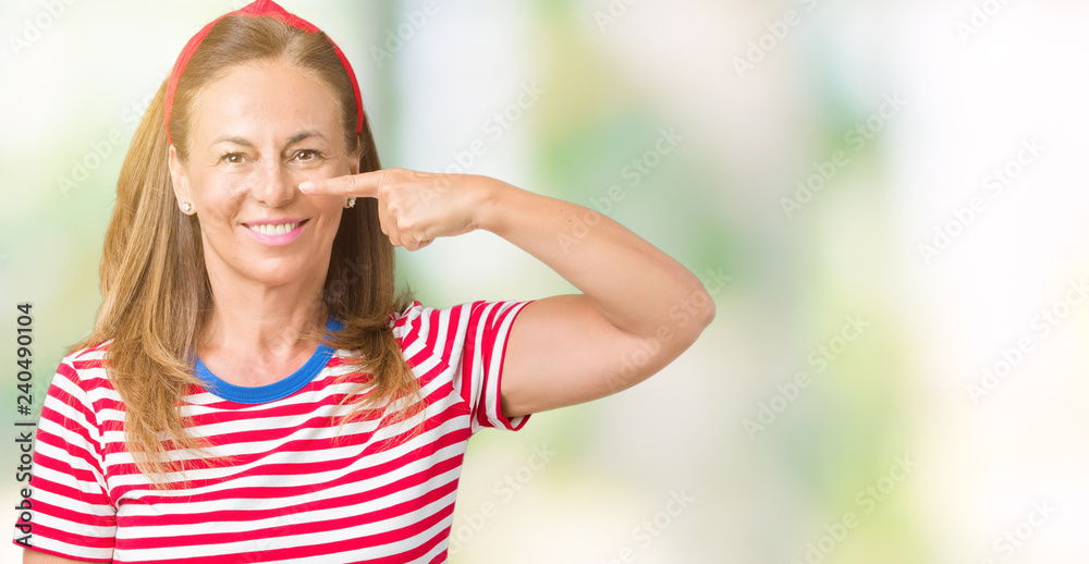 Beautiful middle age woman wearing casual stripes t-shirt over isolated background Pointing with hand finger to face and nose, smiling cheerful Beautiful middle age woman wearing casual stripes t-shirt over isolated background Pointing with hand finger to face and nose, smiling cheerful
