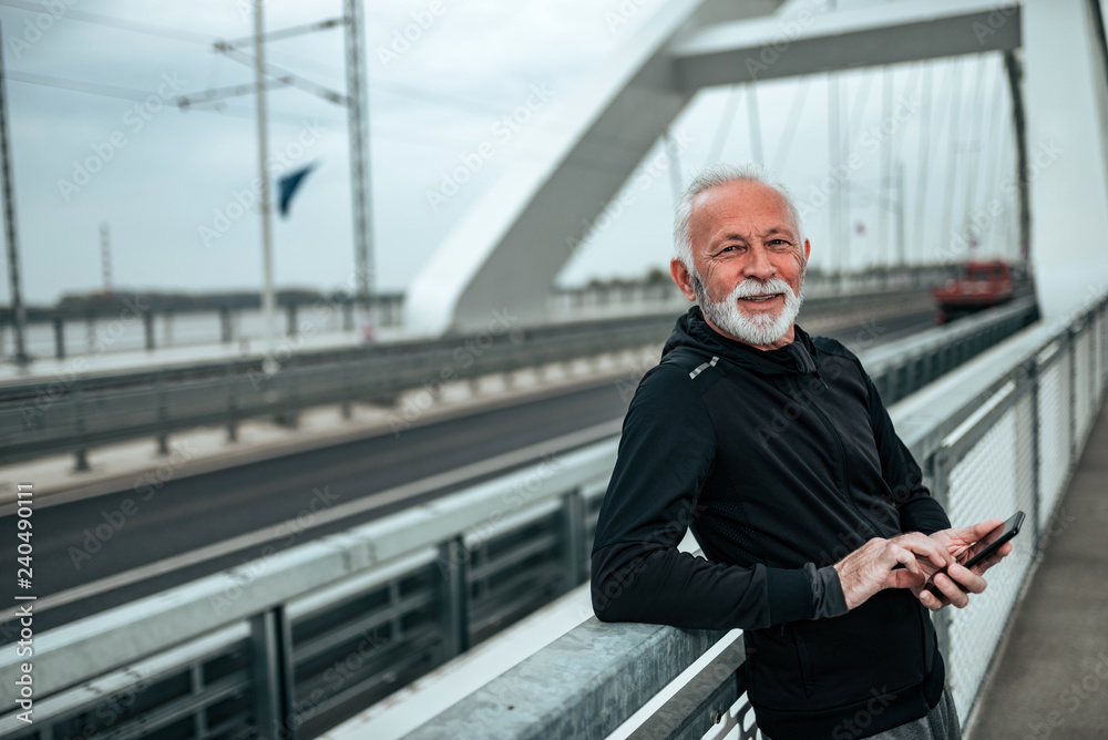 Portrait of senior athlete using phone while standing on the city bridge. Portrait of senior athlete using phone while standing on the city bridge.