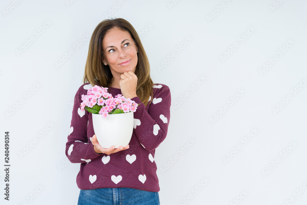 Middle age woman holding flowers pot plant over isolated background serious face thinking about question, very confused idea Middle age woman holding flowers pot plant over isolated background serious face thinking about question, very confused idea