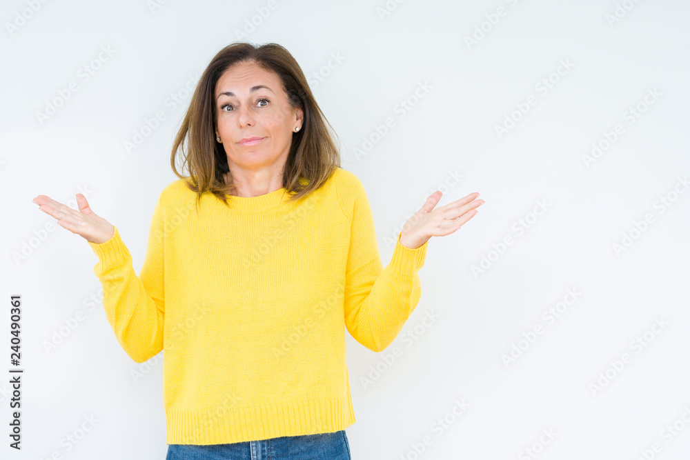Beautiful middle age woman wearing yellow sweater over isolated background clueless and confused expression with arms and hands raised. Doubt concept. Beautiful middle age woman wearing yellow sweater over isolated background clueless and confused expression with arms and hands raised. Doubt concept.