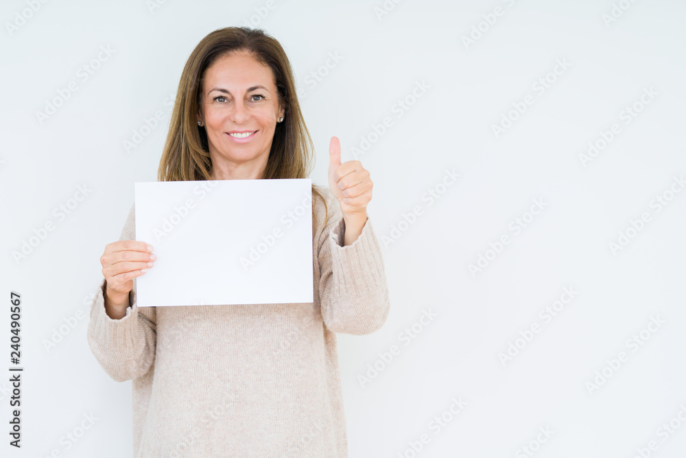 Middle age woman holding blank paper sheet over isolated background happy with big smile doing ok sign, thumb up with fingers, excellent sign Middle age woman holding blank paper sheet over isolated background happy with big smile doing ok sign, thumb up with fingers, excellent sign