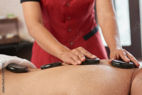 Close-up of male back with hot stones on it and professional doing relaxing massage
