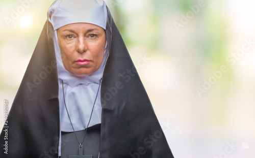 Middle age senior christian catholic nun woman over isolated background with serious expression on face. Simple and natural looking at the camera.