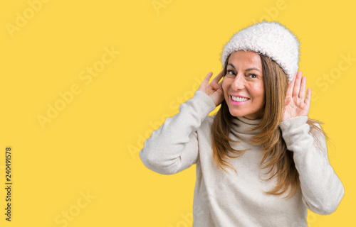 Beautiful middle age woman wearing winter sweater and hat over isolated background Trying to hear both hands on ear gesture, curious for gossip. Hearing problem, deaf © Krakenimages.com