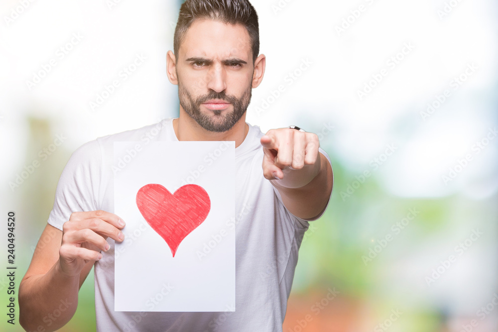 Handsome young man holding card with red heart over isolated background pointing with finger to the camera and to you, hand sign, positive and confident gesture from the front