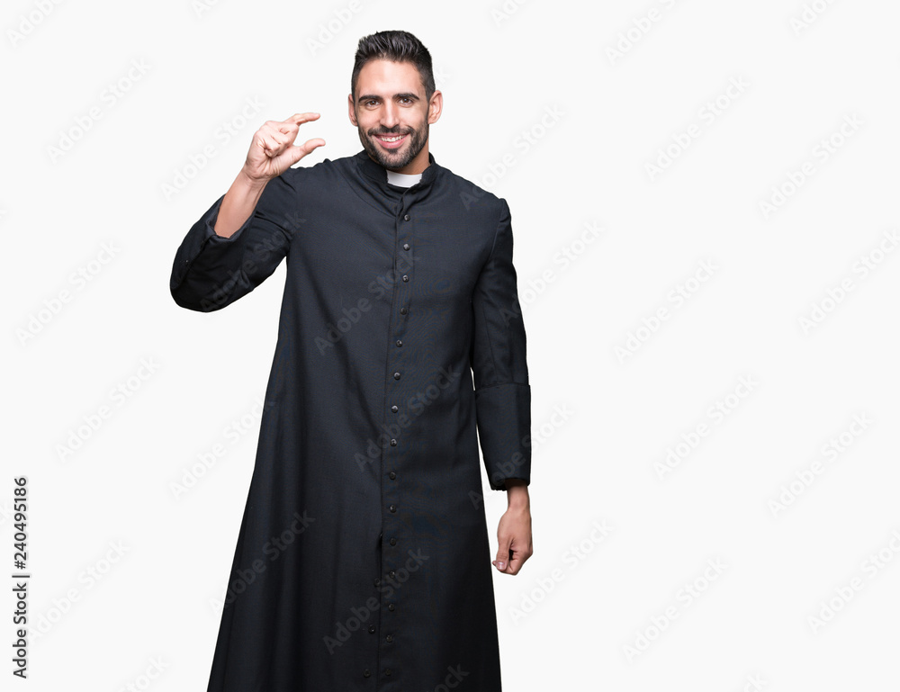 Young Christian priest over isolated background smiling and confident gesturing with hand doing size sign with fingers while looking and the camera. Measure concept.