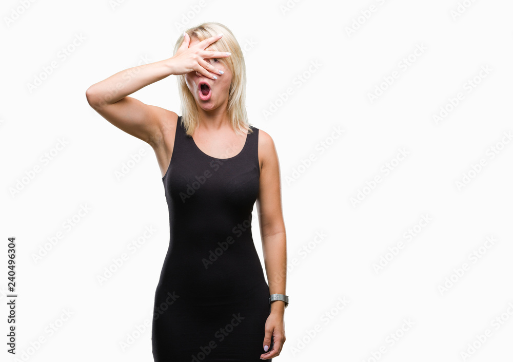 Fototapeta premium Young beautiful blonde attractive woman wearing elegant dress over isolated background peeking in shock covering face and eyes with hand, looking through fingers with embarrassed expression.
