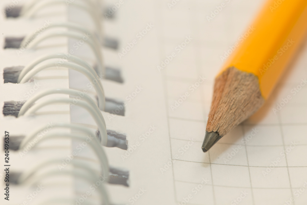 Note book and pencil. a pencil on a white paper in a cell. A simple pencil on a notebook in the cell. School supplies. Note book and pencil. a pencil on a white paper in a cell. A simple pencil on a notebook in the cell. School supplies.