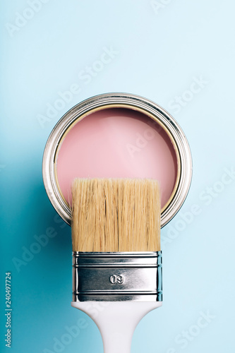 Brush with white handle on open can of pink paint on blue pastel background. Renovation concept. Macro.