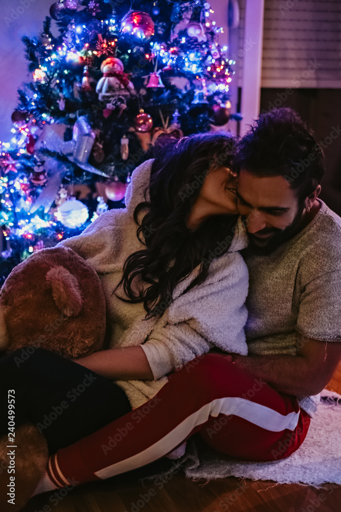 Girl kissing boyfriend in front of Christmas tree
