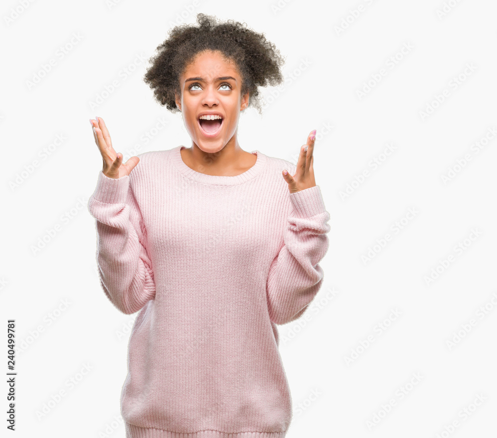 Young afro american woman wearing winter sweater over isolated background crazy and mad shouting and yelling with aggressive expression and arms raised. Frustration concept. Young afro american woman wearing winter sweater over isolated background crazy and mad shouting and yelling with aggressive expression and arms raised. Frustration concept.