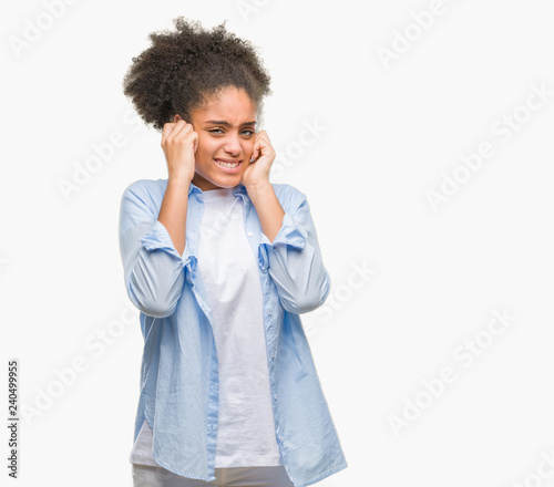 Young afro american woman over isolated background covering ears with fingers with annoyed expression for the noise of loud music. Deaf concept.