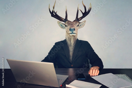 male business man with deer head on a blue background in the office at the Desk. concept of irrational management. stupid employees and employees in the company and morons deputies in the government