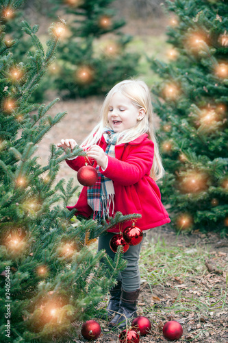 Portrait of happy little girl hanging baubles on tree at farm