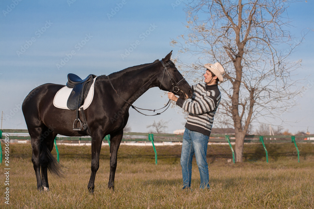 Man nearby horse, striped pullover, blue jeans, hat, landscape Man nearby horse, striped pullover, blue jeans, hat, landscape