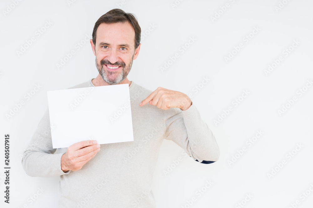 Senior man holding blank paper sheet over isolated background with surprise face pointing finger to himself Senior man holding blank paper sheet over isolated background with surprise face pointing finger to himself