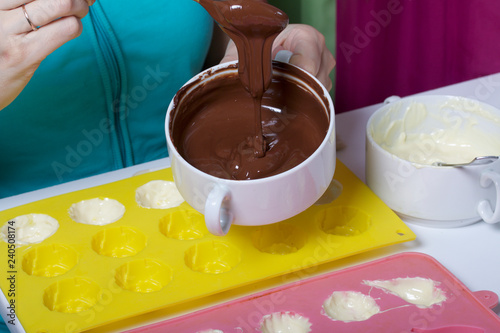 A woman using a brush brushes a silicone dessert mold with a melted black chocolate.
