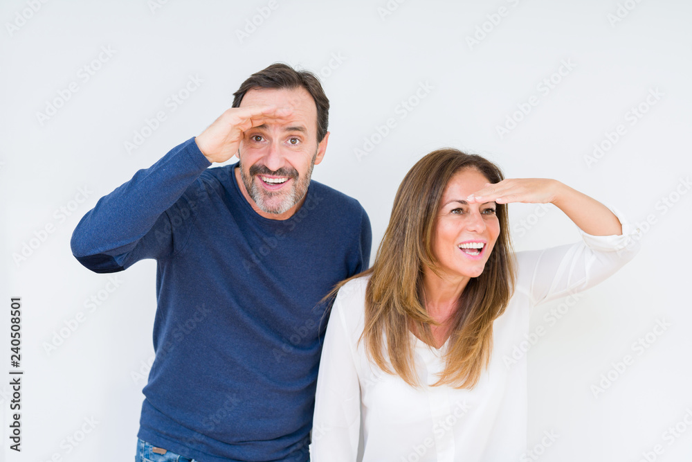 Beautiful middle age couple in love over isolated background very happy and smiling looking far away with hand over head. Searching concept.