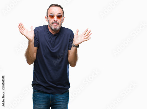 Middle age hoary senior man wearing sunglasses over isolated background clueless and confused expression with arms and hands raised. Doubt concept.