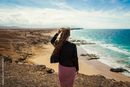 El Cotillo, Fuerteventura, Canary Island, Spain. A young girl is on the top of the cliff and looks at the ocean and cliffs on the horizon. photo