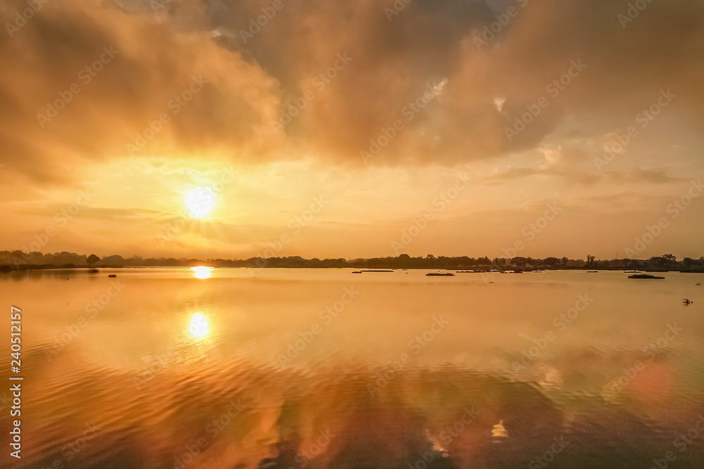 Lake view morning of dark cloud moving above the lake with reflection on the water and colorful of yellow sun light in the sky background, sunrise at Kwan Phayao Lake, Phayao, northern of Thailand.