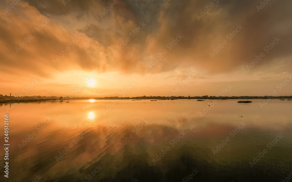 Lake view morning of dark cloud moving above the lake with reflection on the water and colorful of yellow sun light in the sky background, sunrise at Kwan Phayao Lake, Phayao, northern of Thailand.