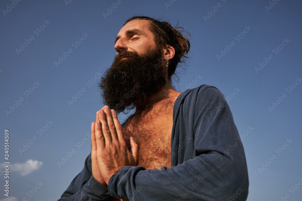 handsome bearded male with namaste hands in blue clear sky background