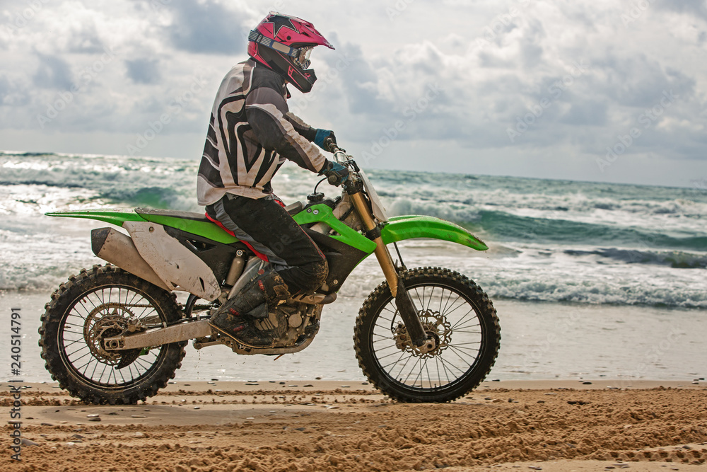 Motorcyclist in a protective suit rides on one wheel of motorcycle on the sea, splashes fly from under the wheels. Motorcyclist in a protective suit rides on one wheel of motorcycle on the sea, splashes fly from under the wheels.