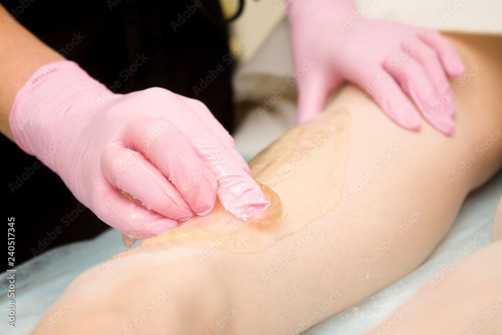 Naklejka premium procedure of hair removing on leg beautiful woman with sugar paste or wax honey and pink gloves hand - depilation and beauty concept